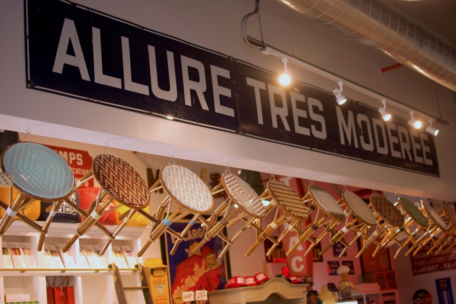 Large French sign that reads ALLURE TRES MODEREE with a collection of small stools beneath it.